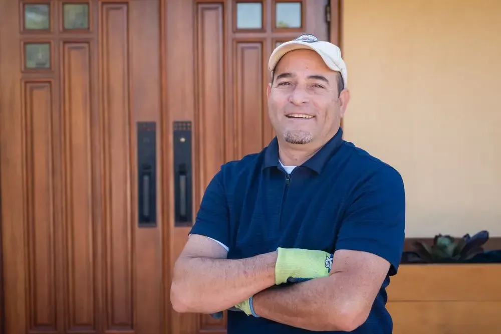 A man is standing in front of a wooden door with his arms crossed.