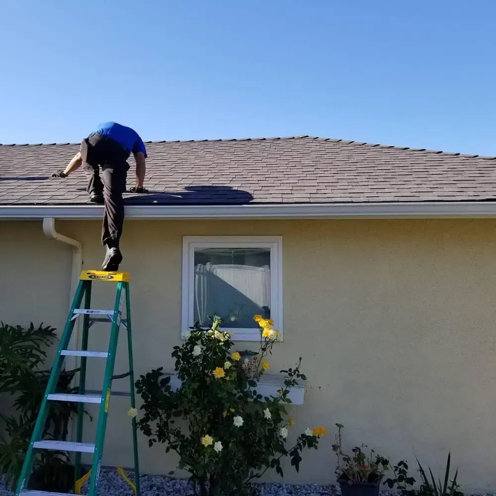 A man is standing on a ladder on the roof of a house.