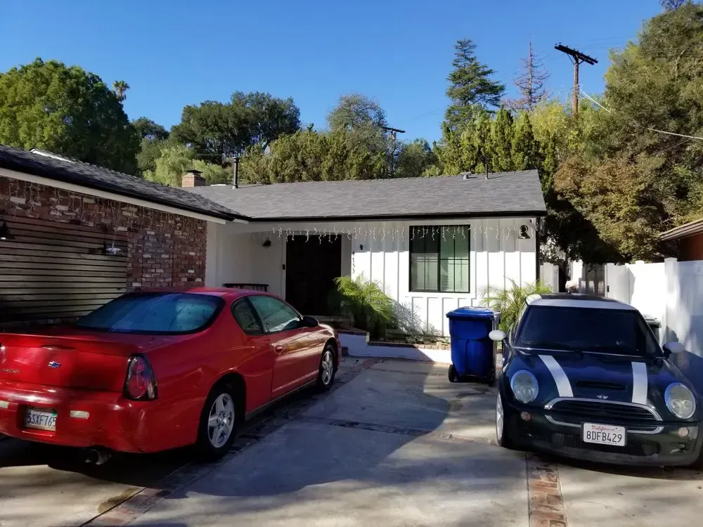 A red car and a black car are parked in front of a house.