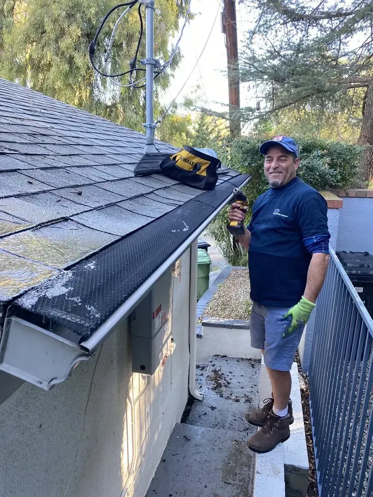 A man is standing next to a gutter on the side of a house.