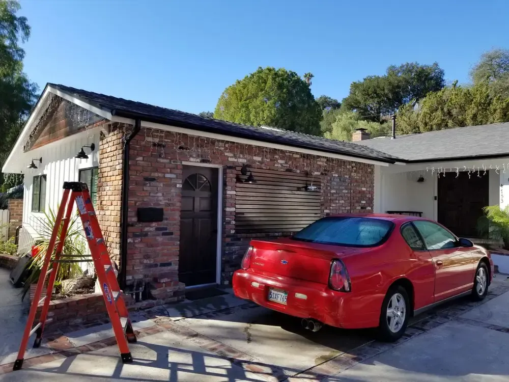 A red car is parked in front of a brick house.