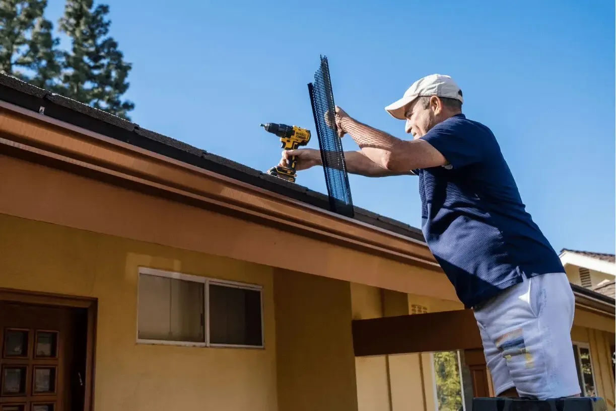 A man is working on the roof of a house with a drill.