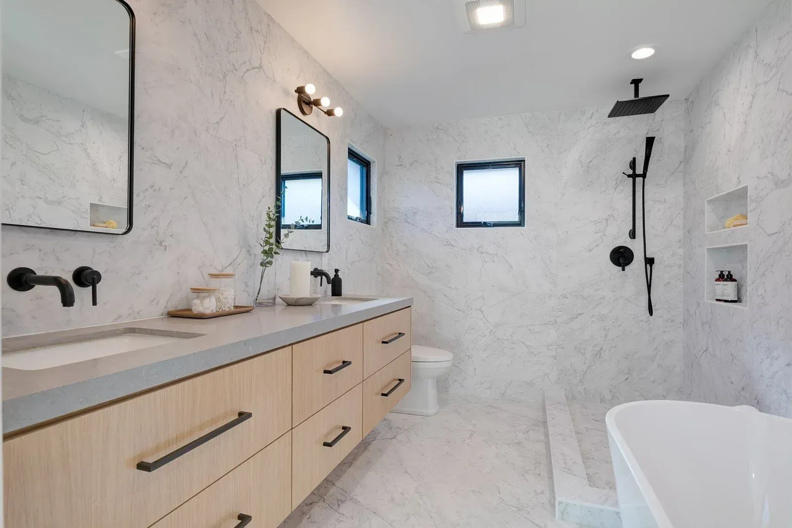 Modern bathroom with white marble walls, wooden vanity, black fixtures.