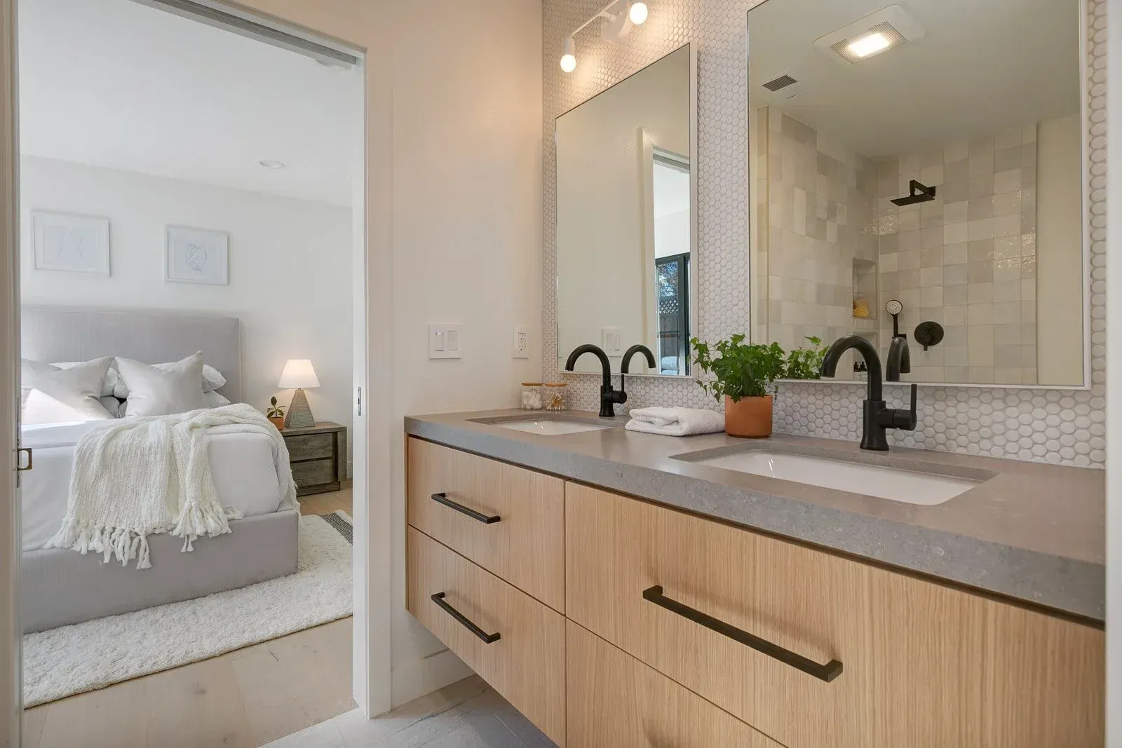 Bathroom with double vanity and adjacent bedroom view. Light wood cabinets, black fixtures.
