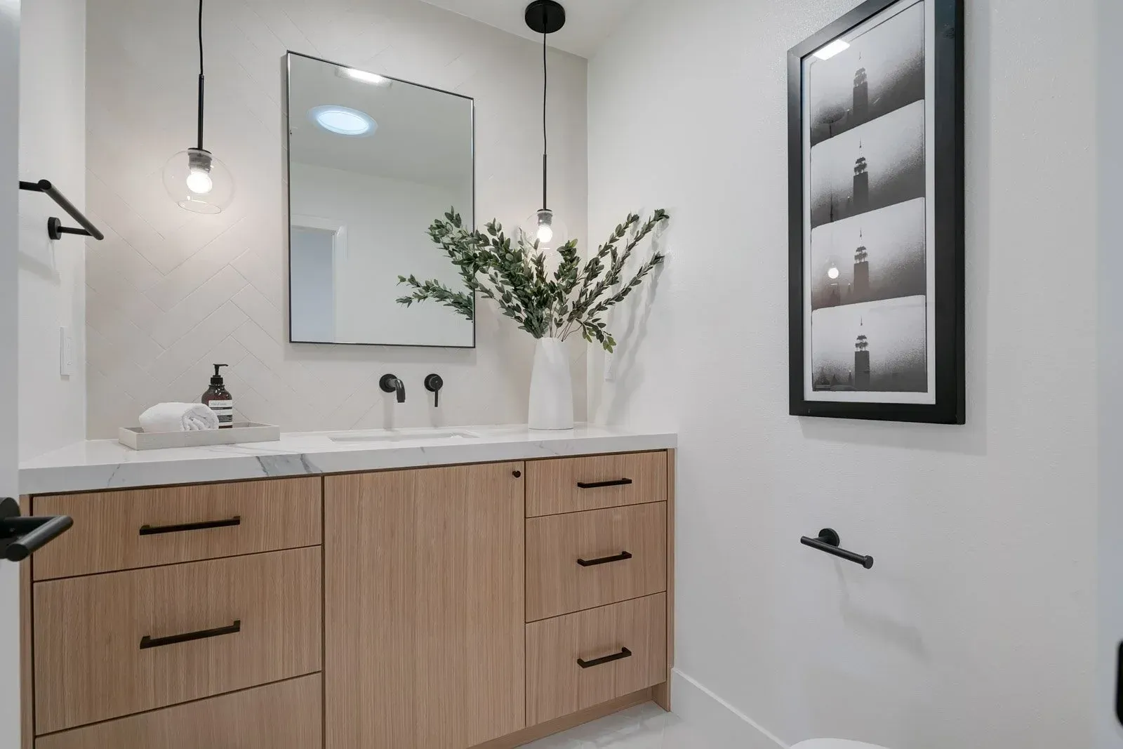 Modern bathroom with light wood vanity, black fixtures, and white walls.