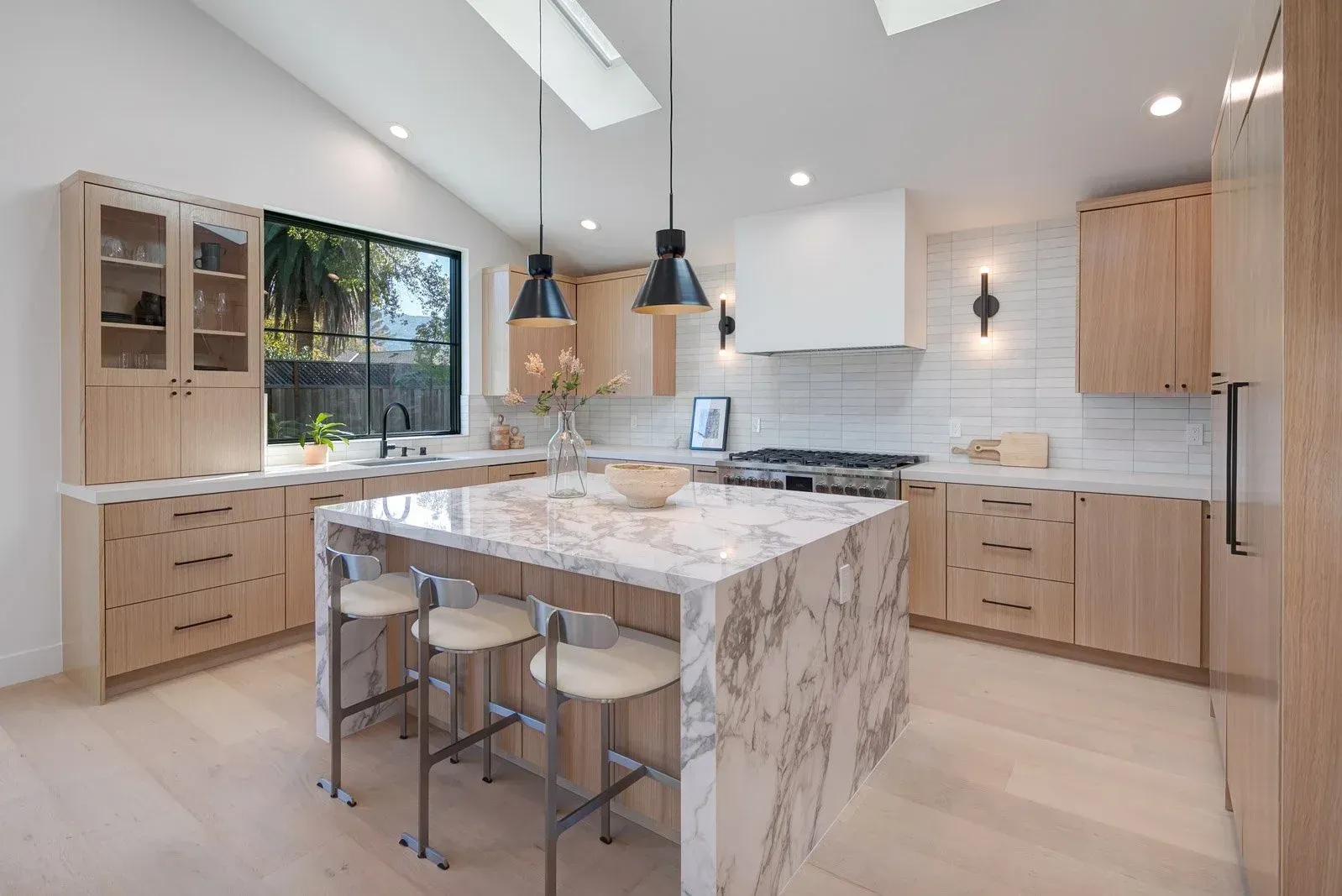 Modern kitchen with light wood cabinets, marble island, and skylights.