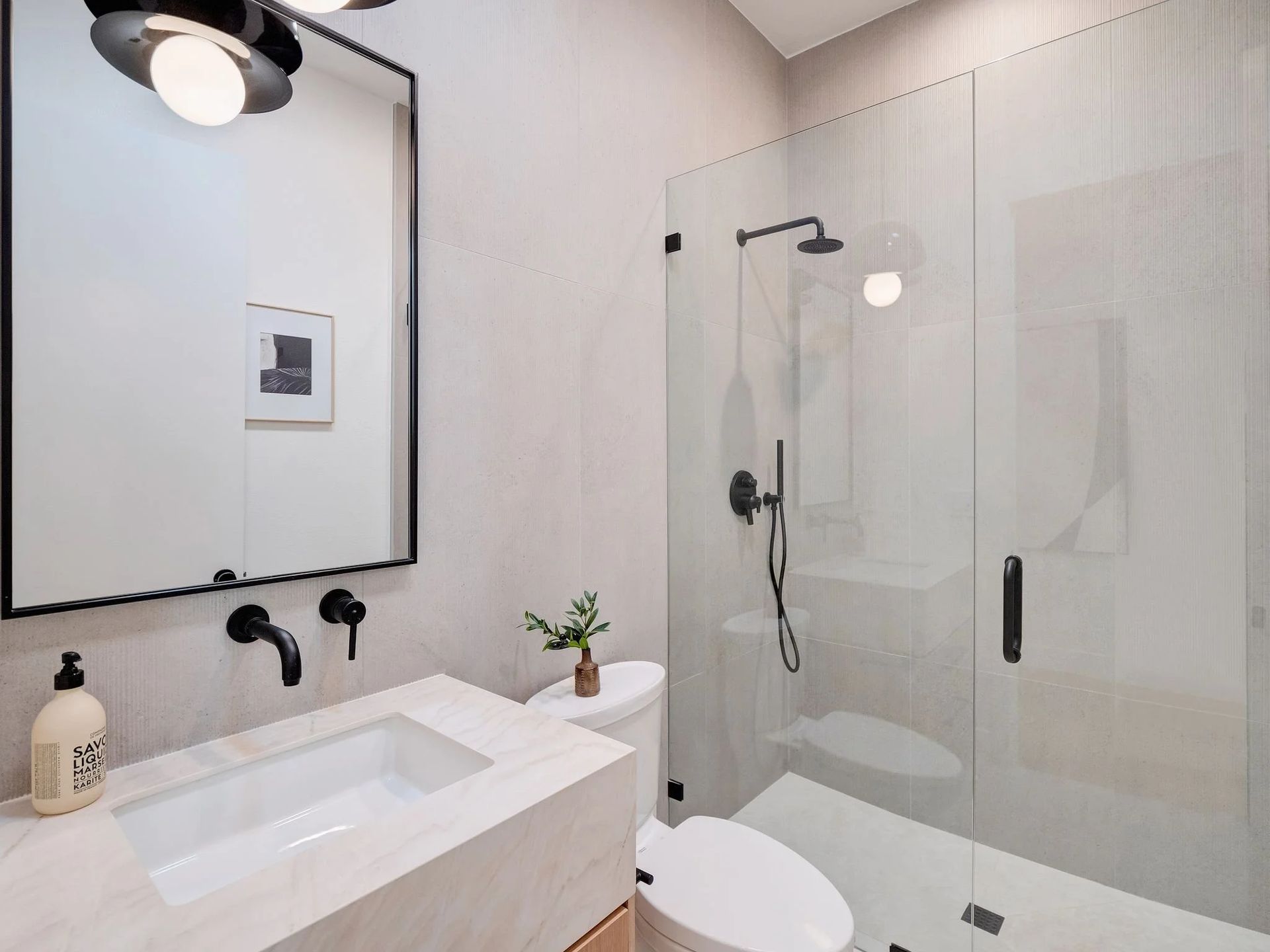 Modern bathroom with white walls, glass shower, black fixtures, and vanity.