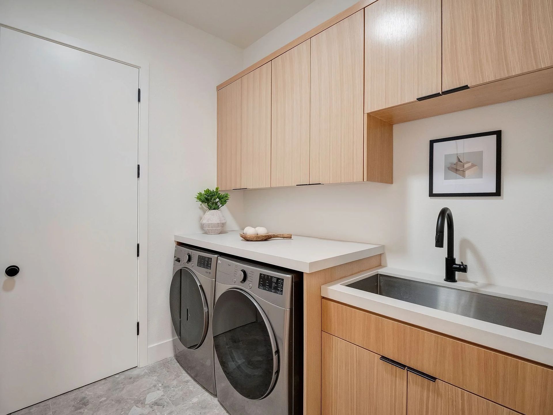 Laundry room with light wood cabinets, white countertop, stainless steel sink, and washing machine.