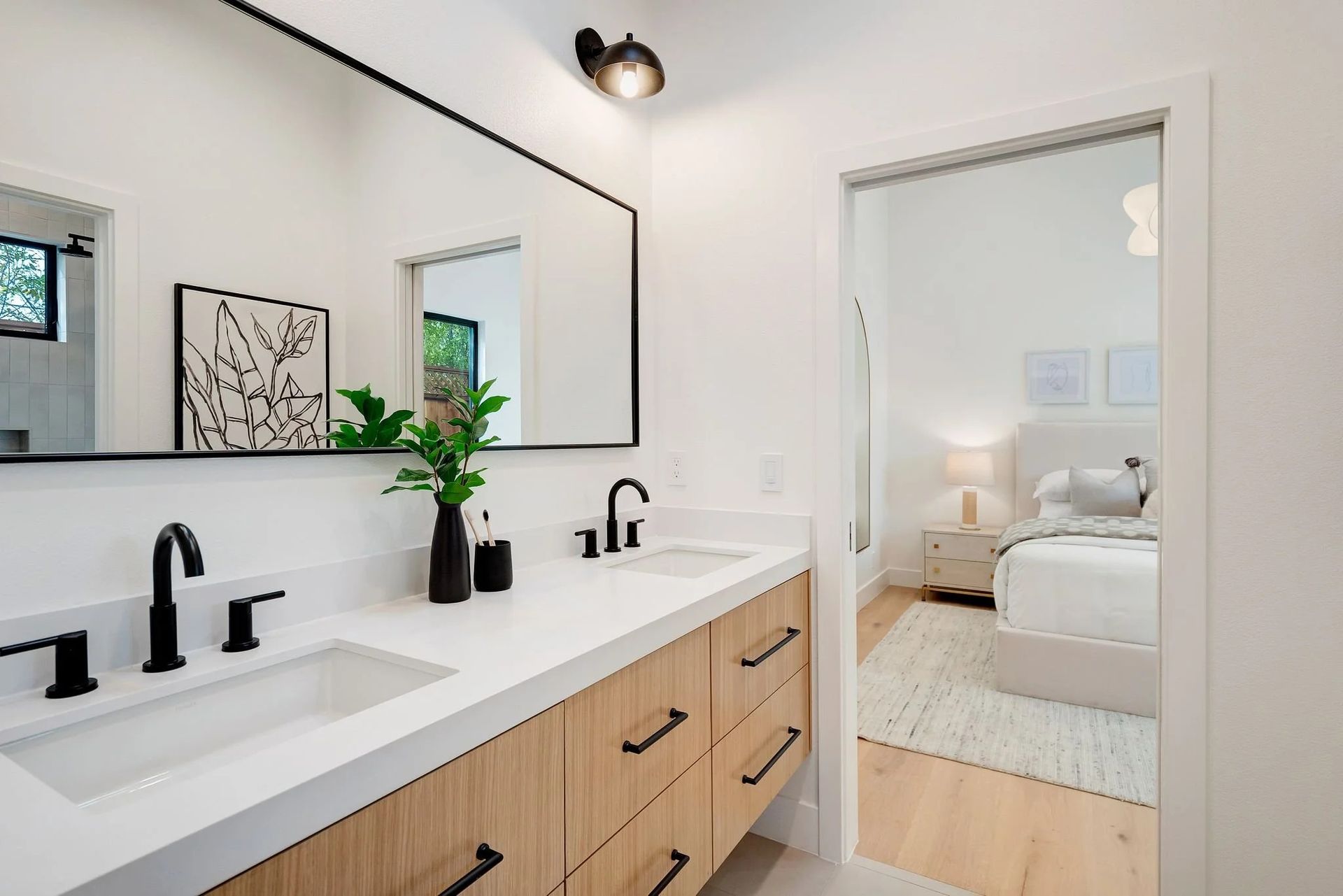 Modern bathroom with double sinks, wood vanity, and a view into a bedroom.