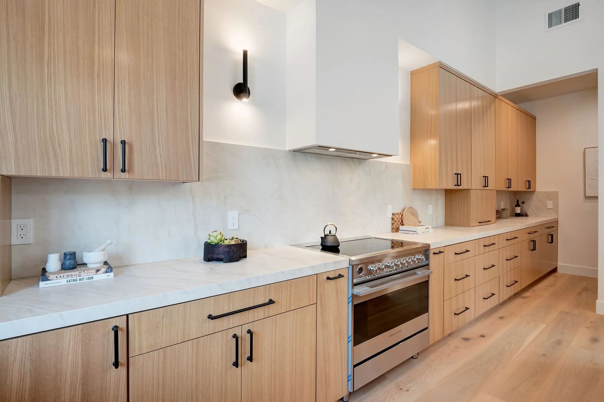 Modern kitchen with light wood cabinets, stainless steel stove, and white countertops.