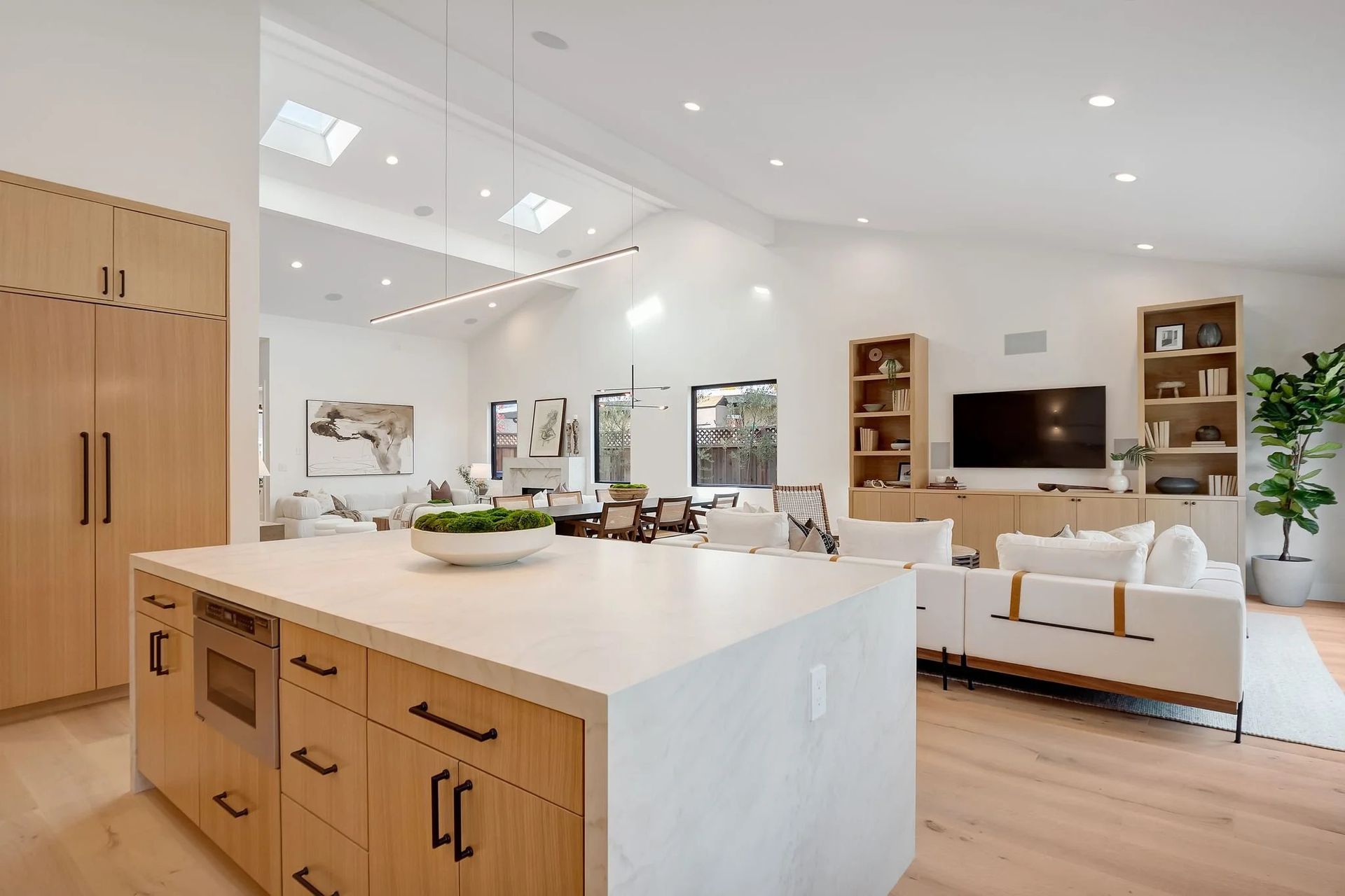 Modern kitchen with light wood cabinets, island, and open living area.