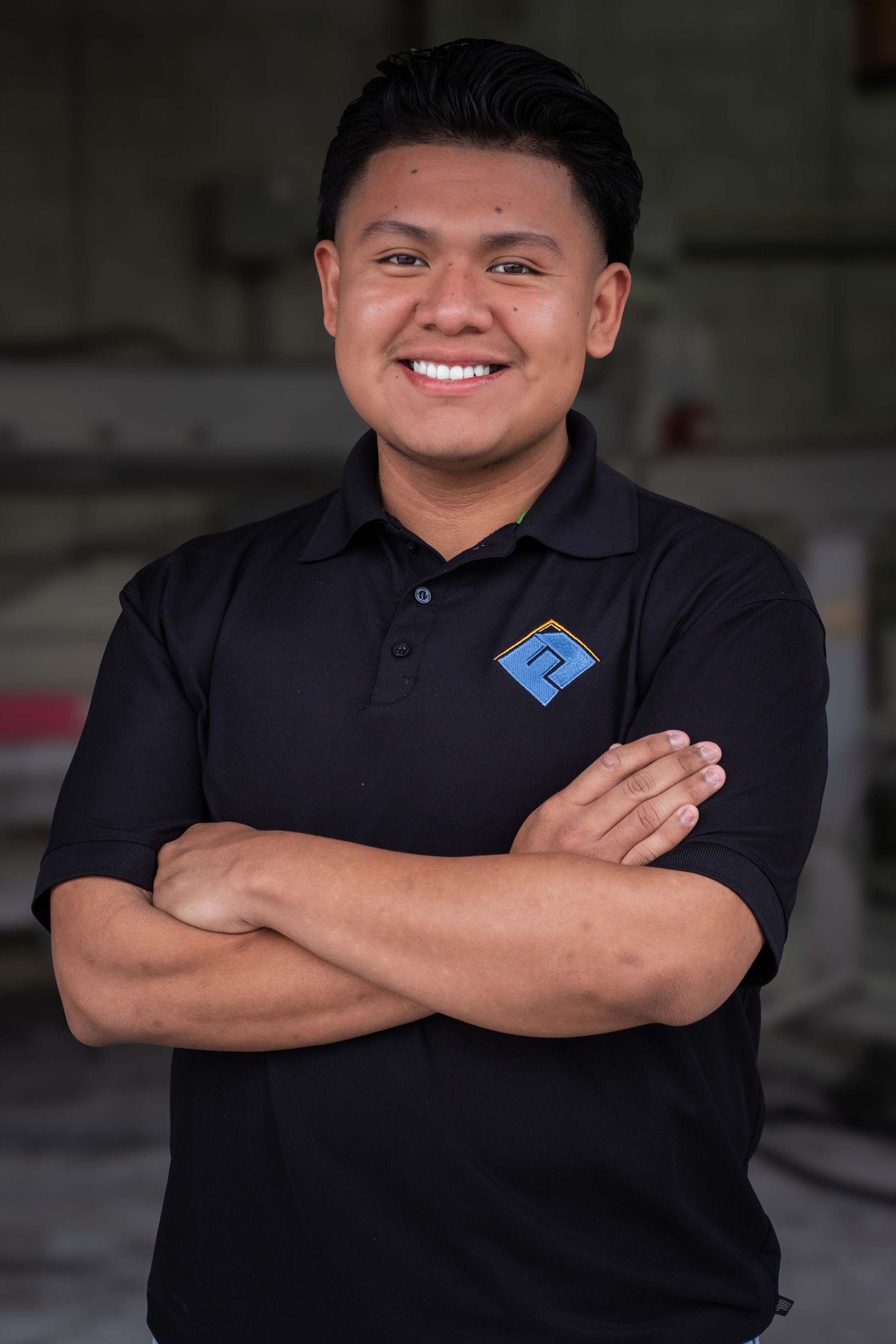 Man with crossed arms smiles, wearing a black polo shirt.