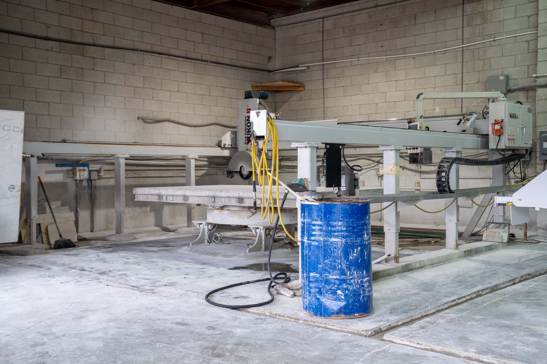 A large industrial stone cutting machine in a dusty warehouse with a blue barrel in the foreground.