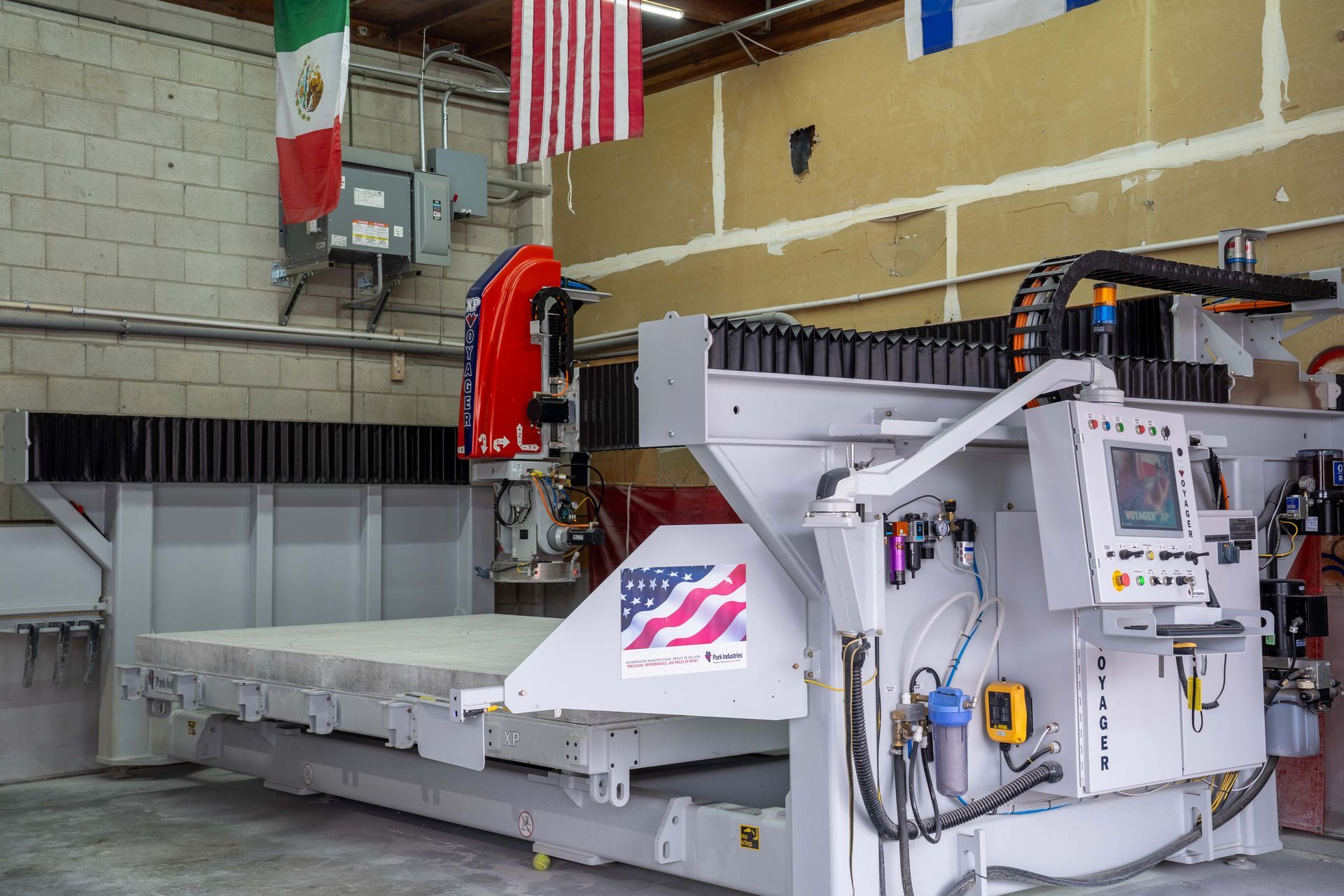 A large, industrial CNC machine with a US flag and Mexican flag in a factory setting.