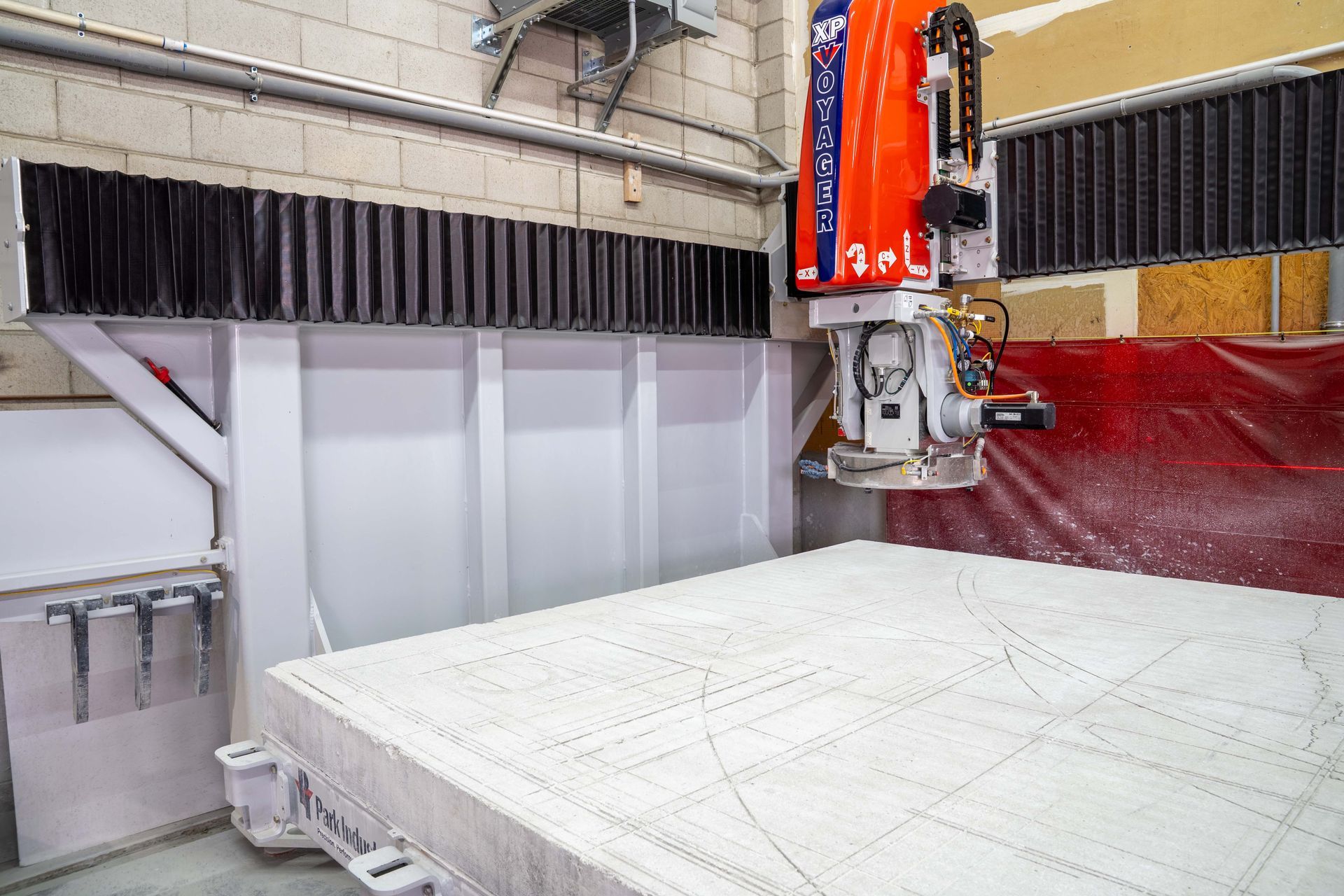 Large white CNC machine carving a pattern into a white surface in a workshop.