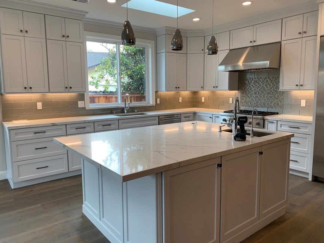 White kitchen with island and cabinets, stainless steel appliances, and window.