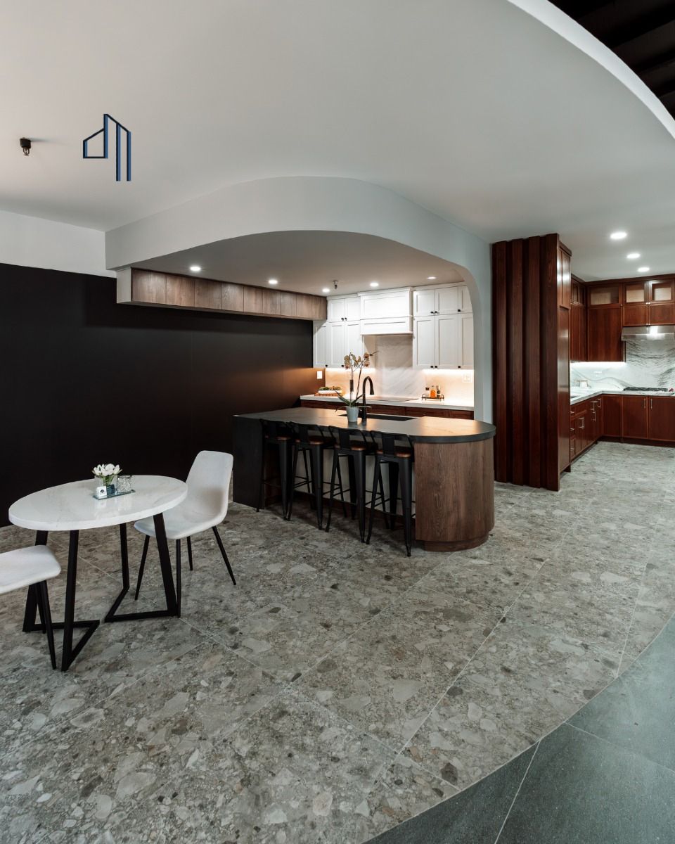 Reception desk in showroom. Curved brown base, light-colored top, computer, and two chairs under a circular recessed ceiling with lights.