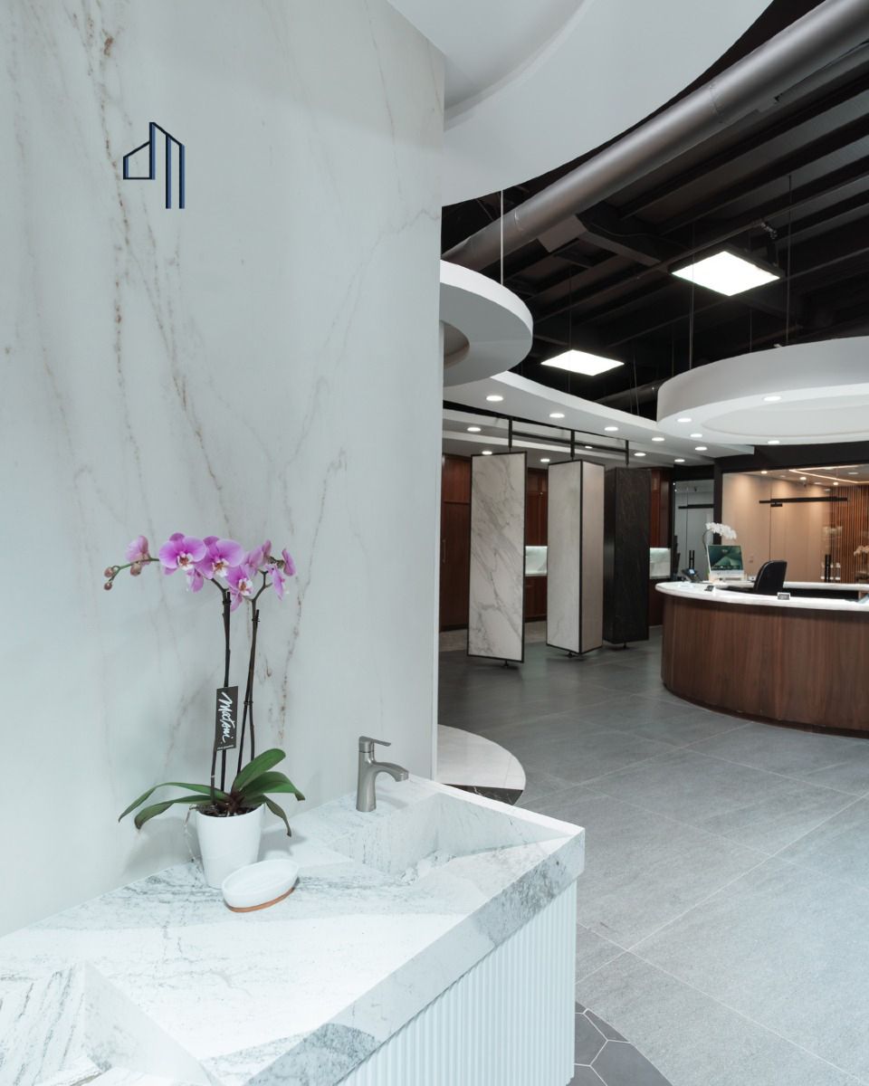 Reception desk in showroom. Curved brown base, light-colored top, computer, and two chairs under a circular recessed ceiling with lights.
