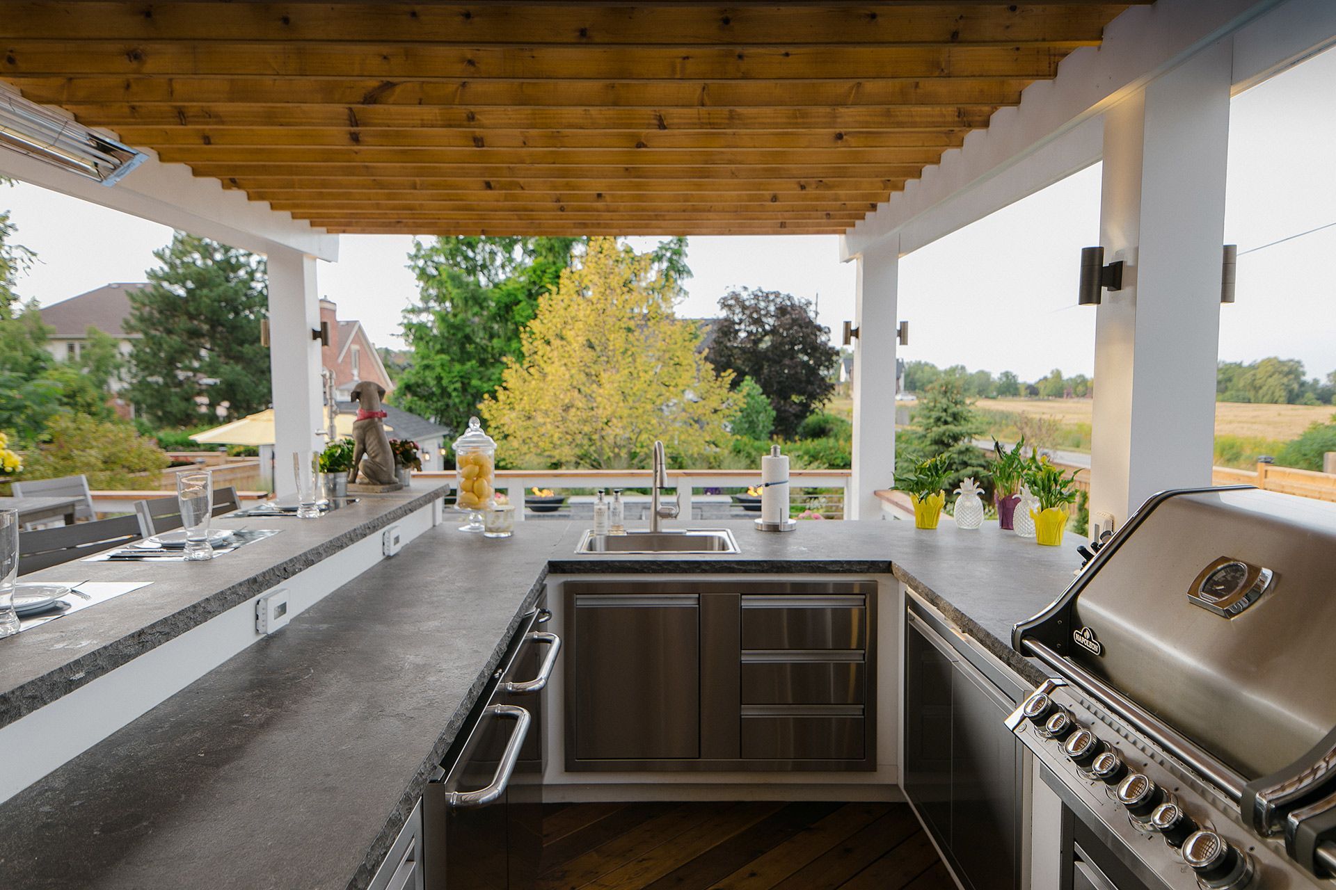 Outdoor kitchen with countertops, sink, grill, and pergola. Overlooks a green landscape.