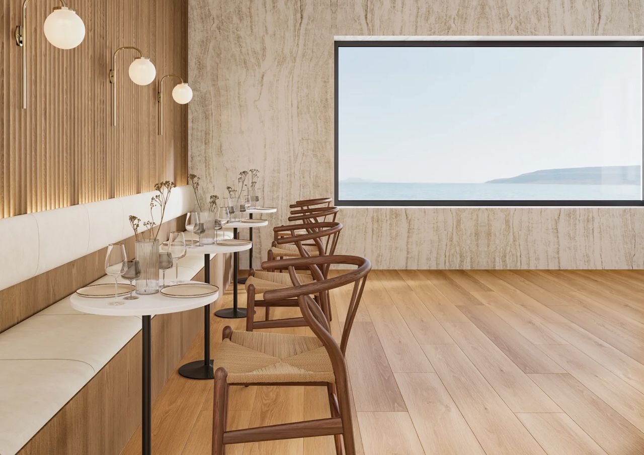 Restaurant interior: wooden floors, tables set for dining, large window with a sea view.