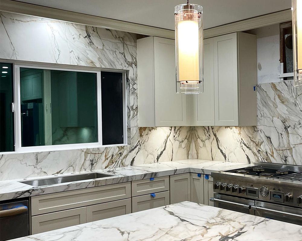 Kitchen with marble countertops and backsplash, light cabinets, and stainless steel appliances.