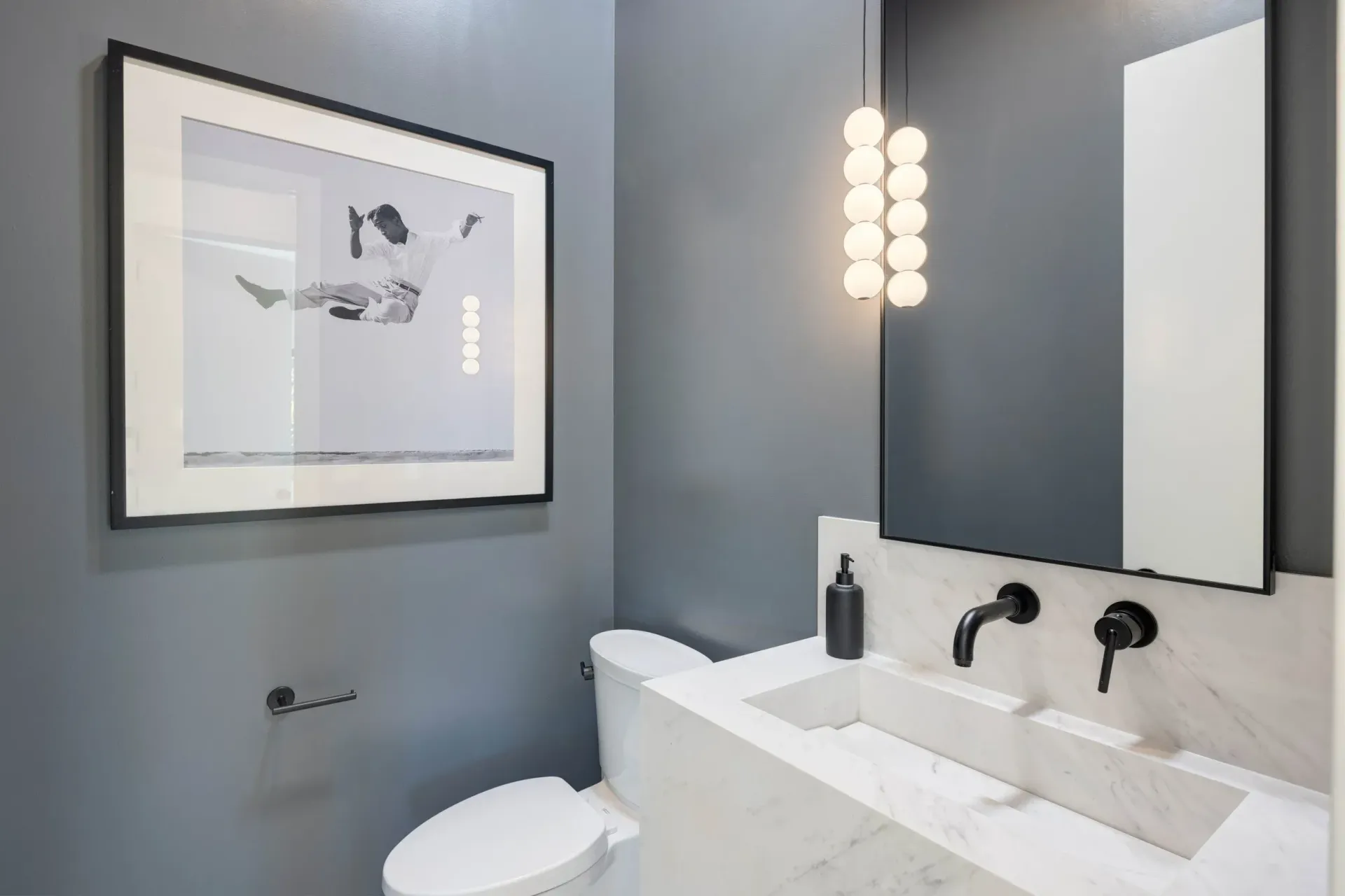 Powder room with gray walls, marble sink, black fixtures, and framed art.