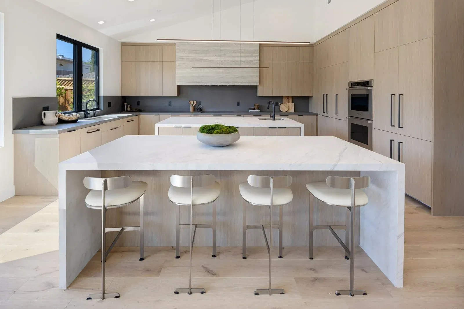 Modern kitchen with light wood cabinets, a large island with stools, and a double oven.