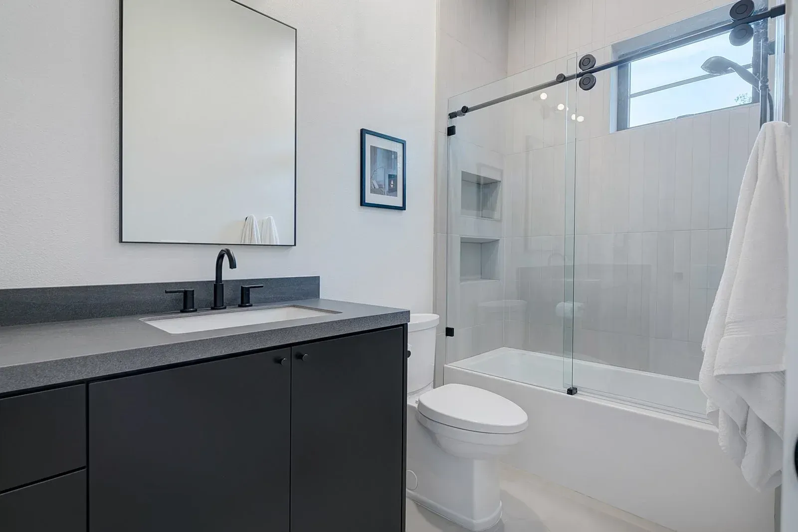 Modern bathroom with a dark gray vanity, glass shower, and white walls.