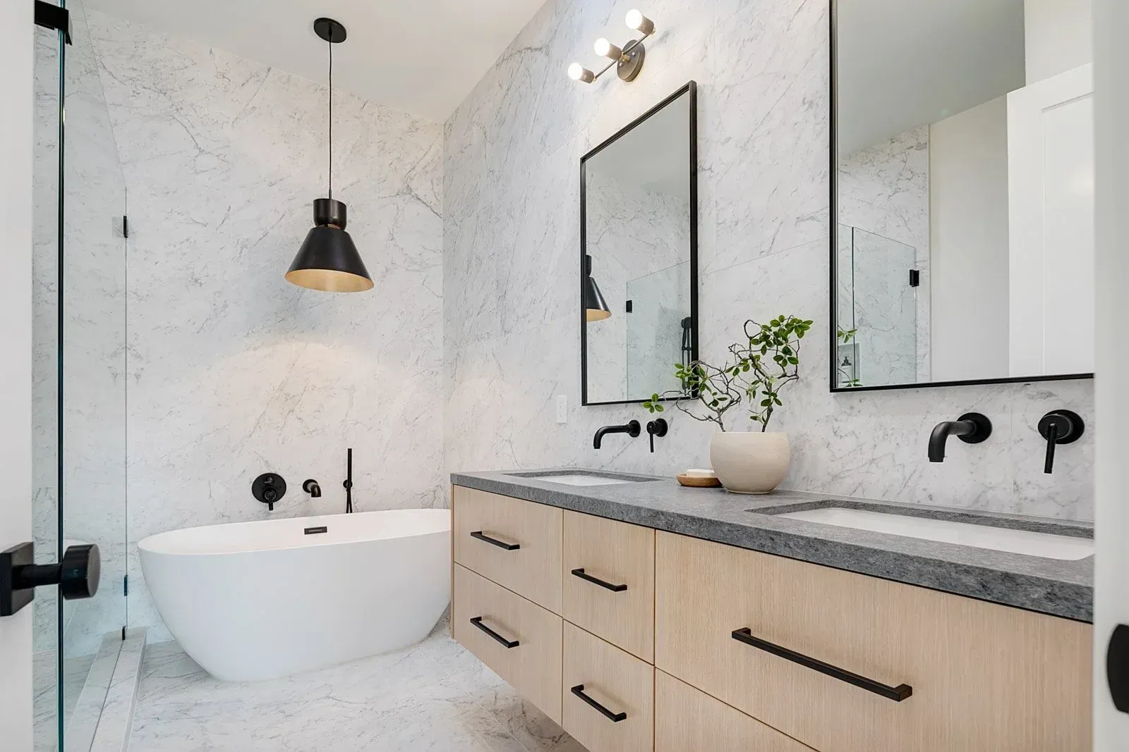 Modern bathroom with a white soaking tub, light wood vanity, and black fixtures.
