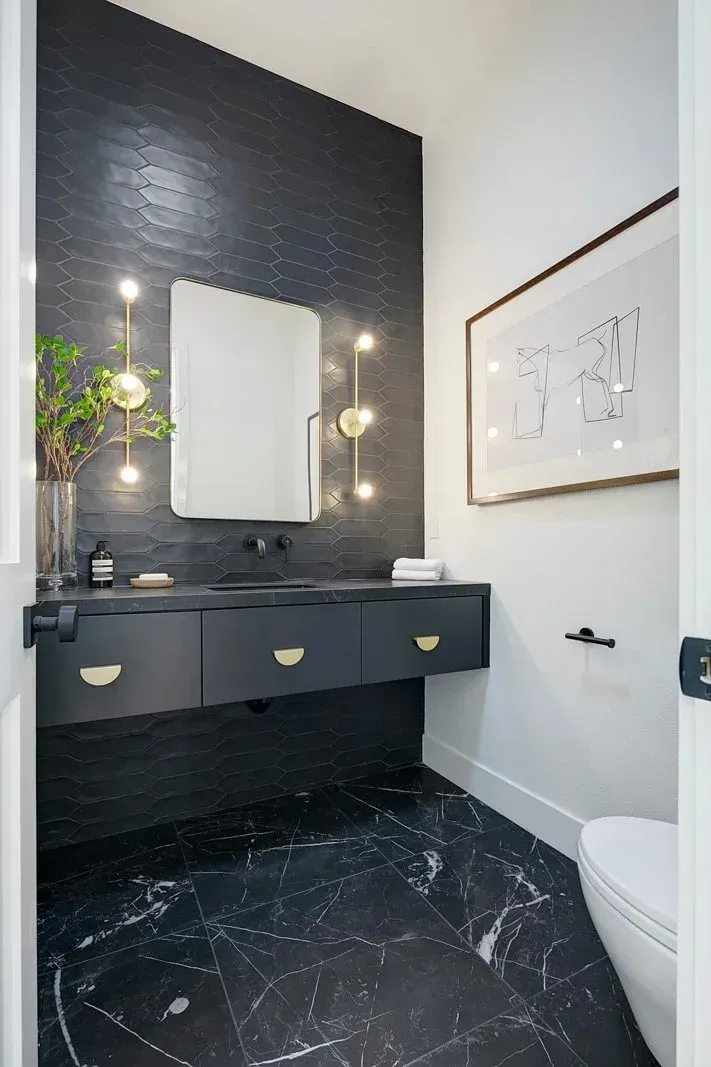 Dark bathroom with black vanity and marble floor, white walls, art, and a toilet.