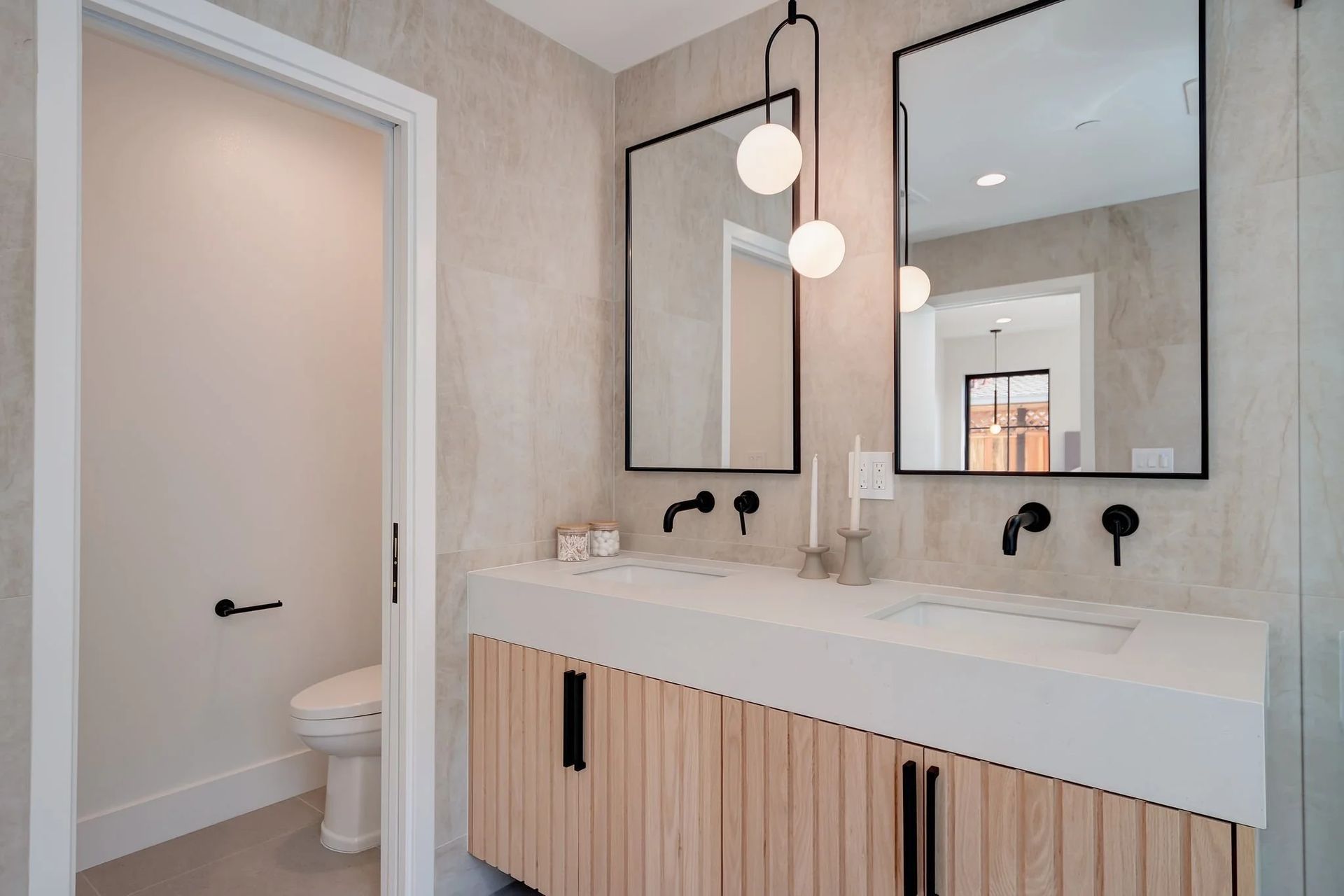 Modern bathroom with double sinks, two black-framed mirrors, and a light wood vanity.