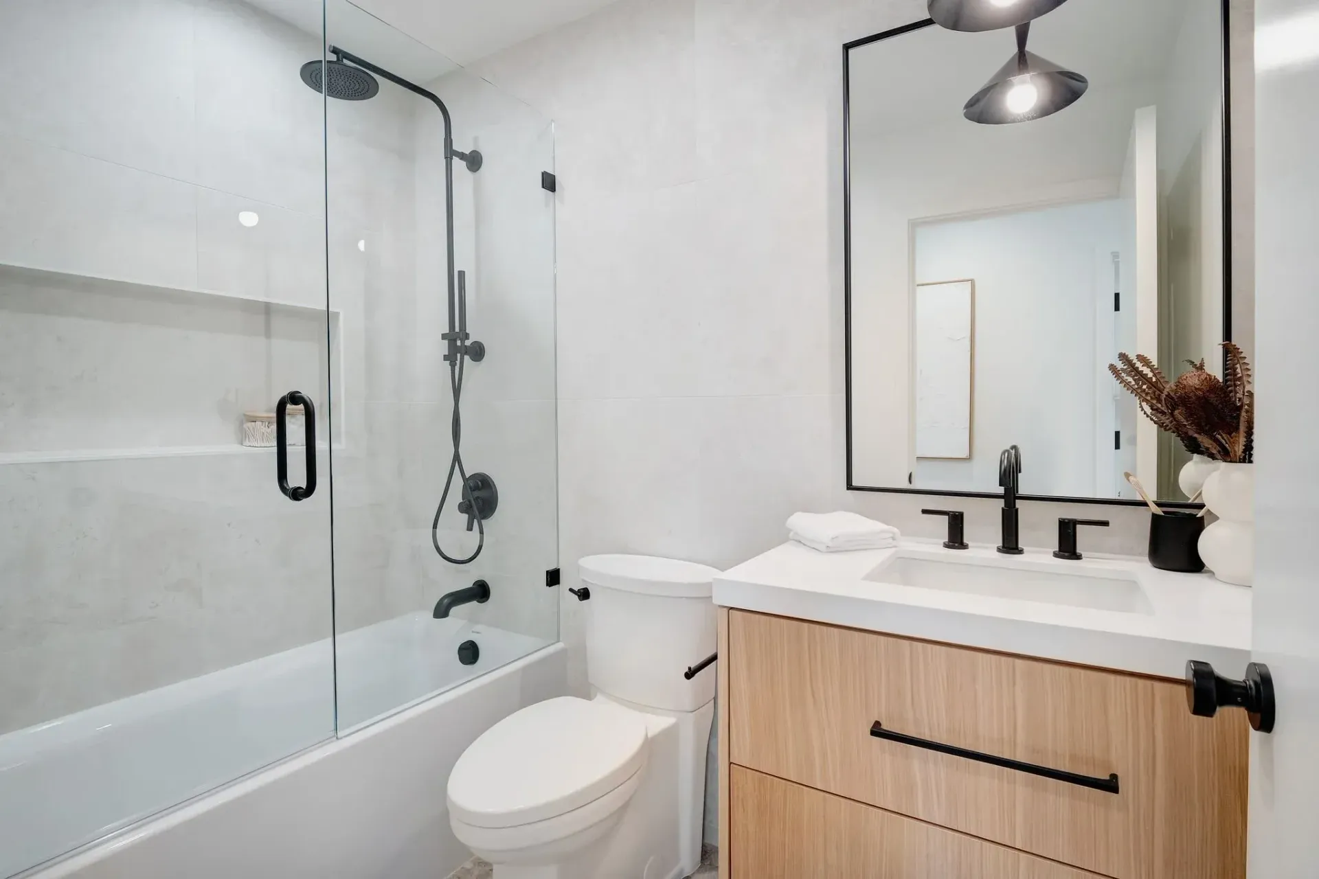 Modern bathroom with a white tub, toilet, and vanity with a wood cabinet.