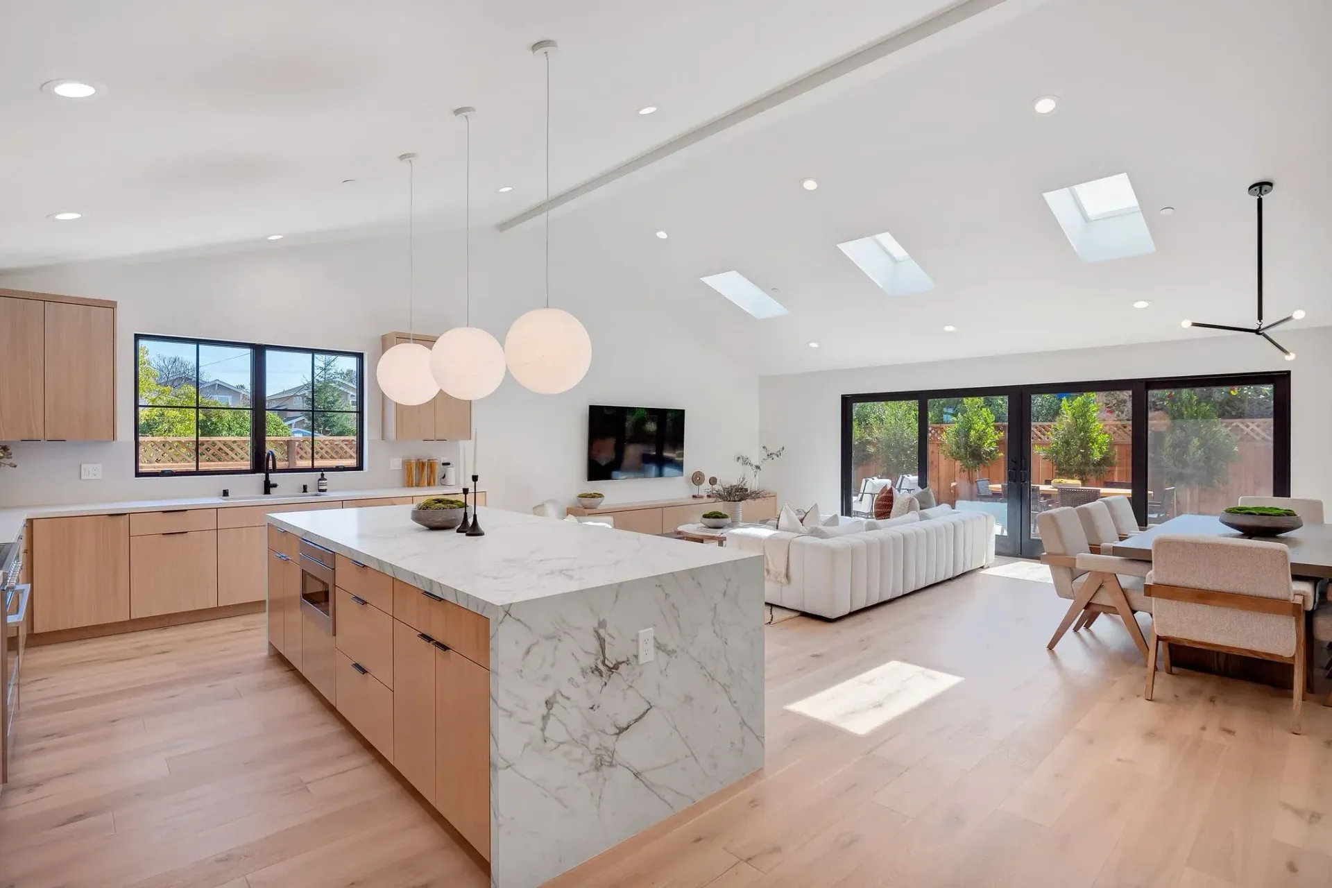 Open-plan kitchen and living area with light wood cabinets, white counters, and skylights.