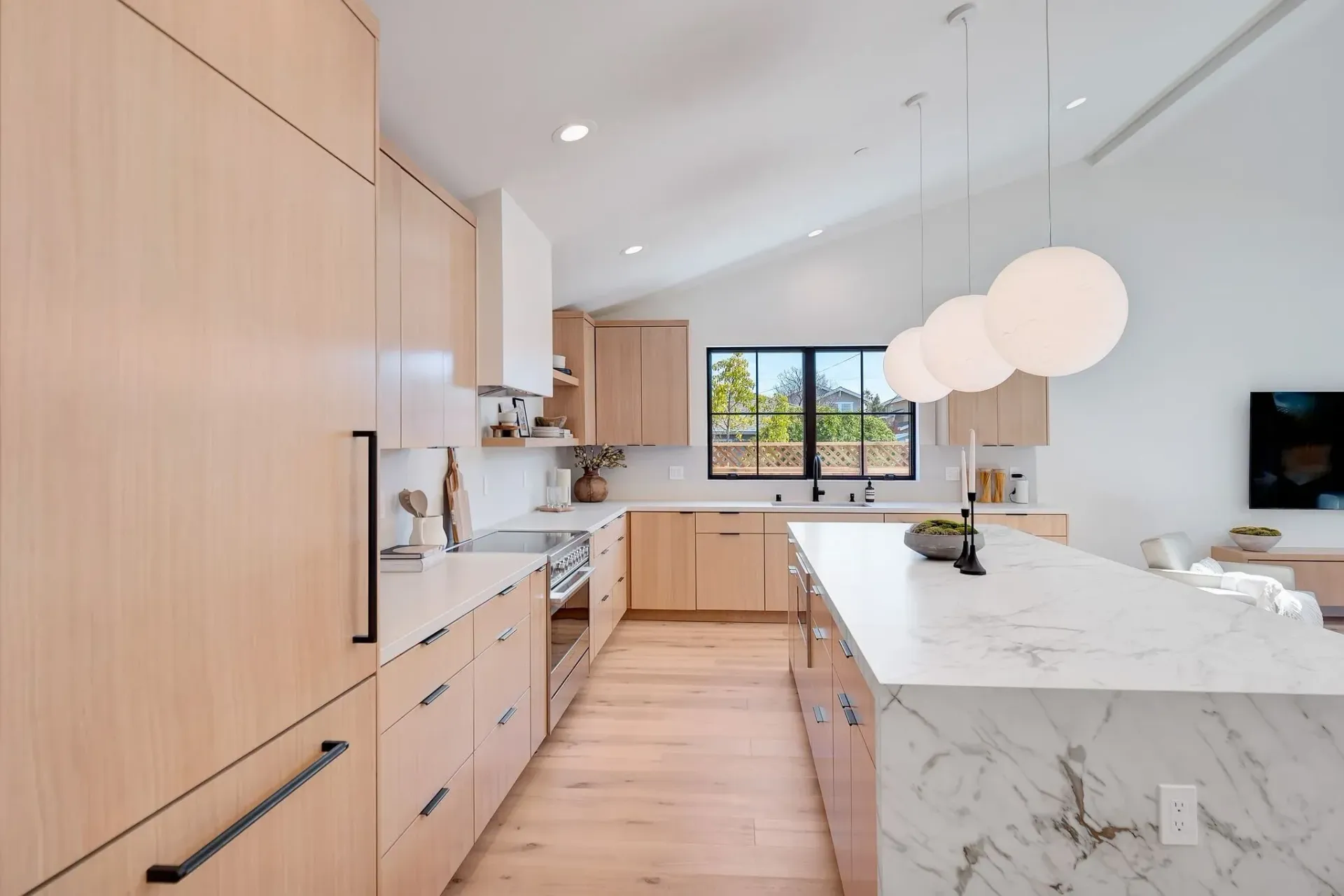 Modern kitchen with light wood cabinets, marble island, and spherical pendant lights.