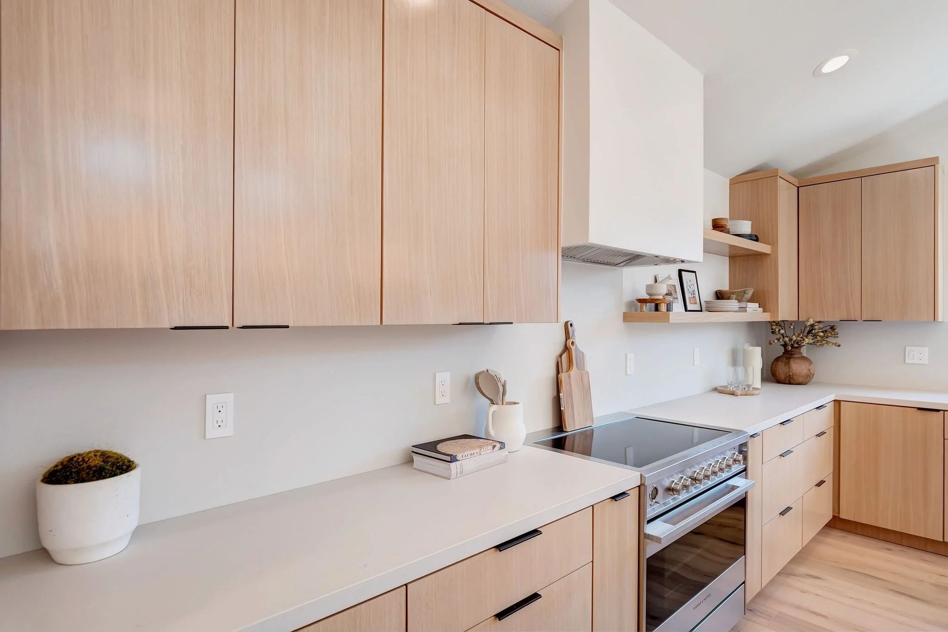 Modern kitchen with light wood cabinets, white countertops, and a stainless steel range.