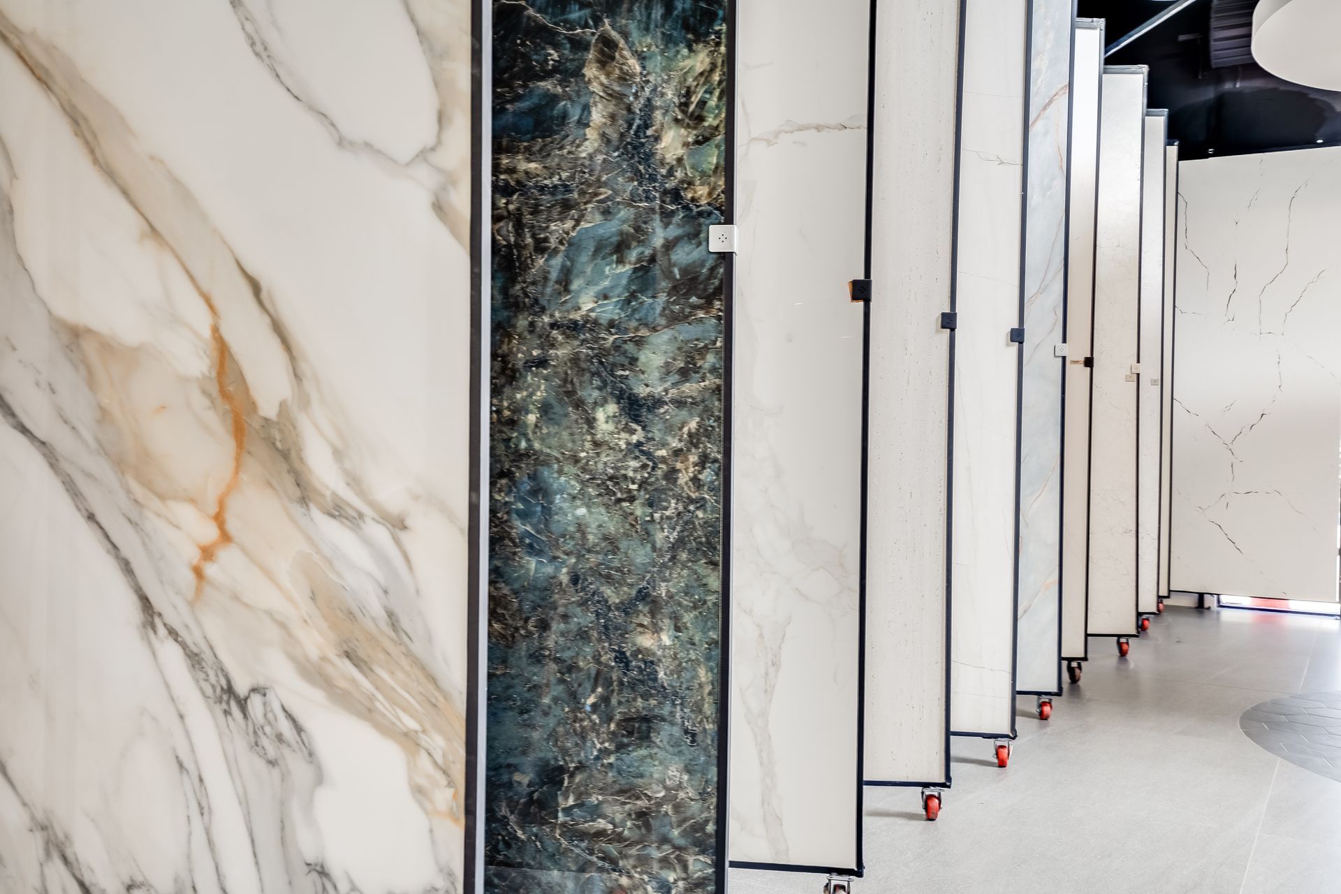 Tile samples displayed on rolling racks in a showroom; various colors and patterns, including marble and abstract designs.