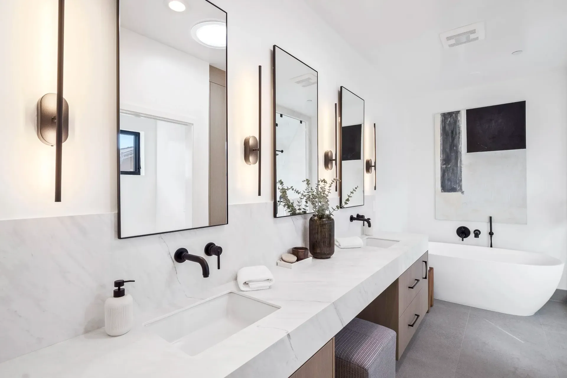 Modern white bathroom with long vanity, mirrors, and a freestanding tub.