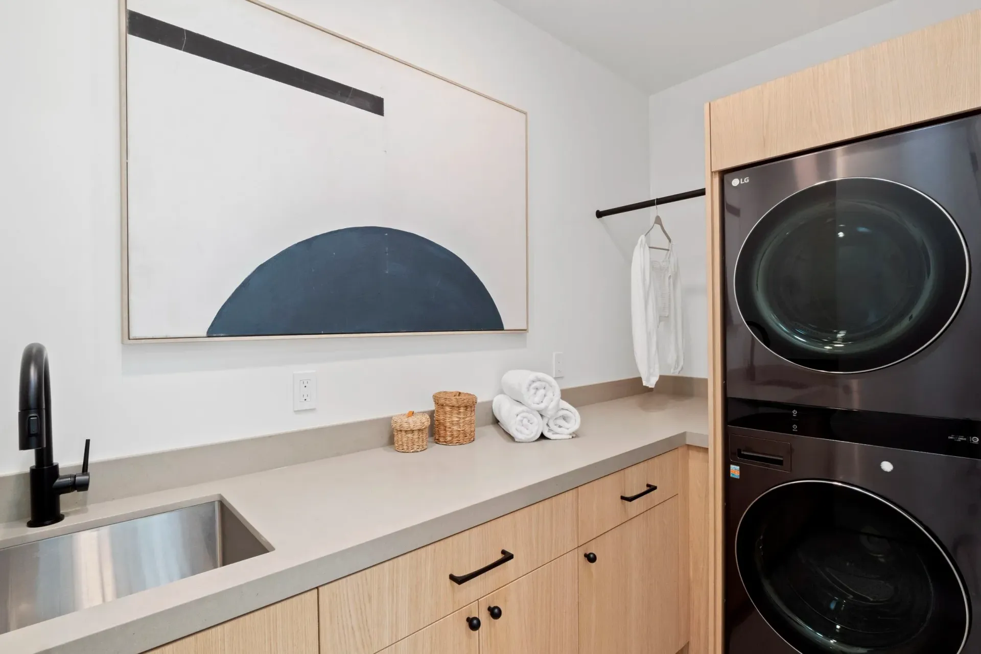 Laundry room with stacked washer/dryer, sink, counter, and abstract art.