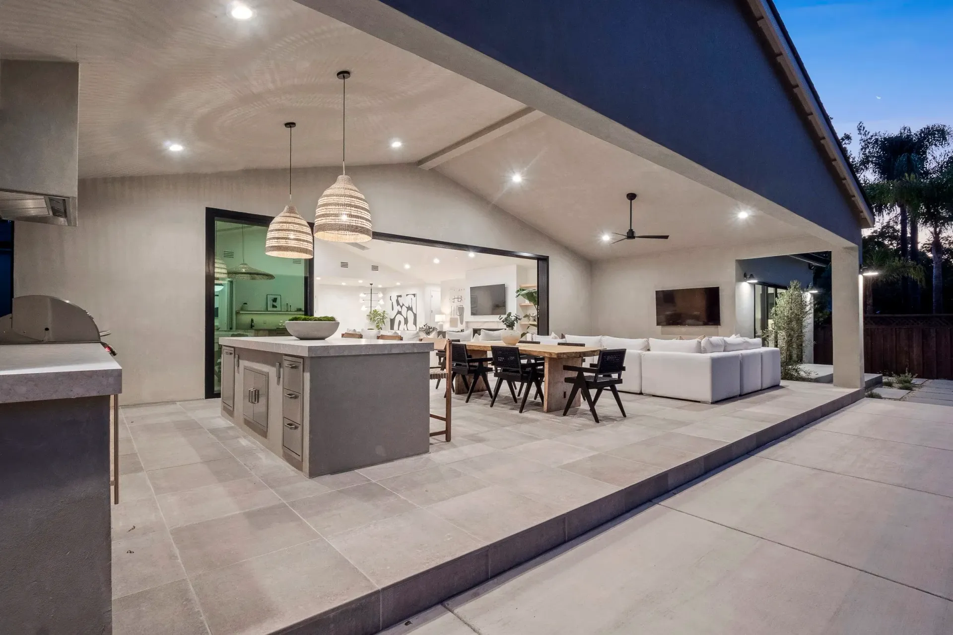Outdoor kitchen and dining area with grey tiles, island, table, and seating.
