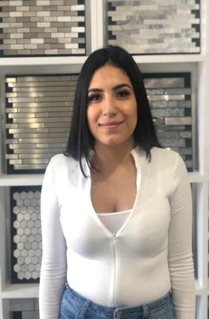 Woman with dark hair wearing a white zip-up shirt and jeans smiles in a tile store.