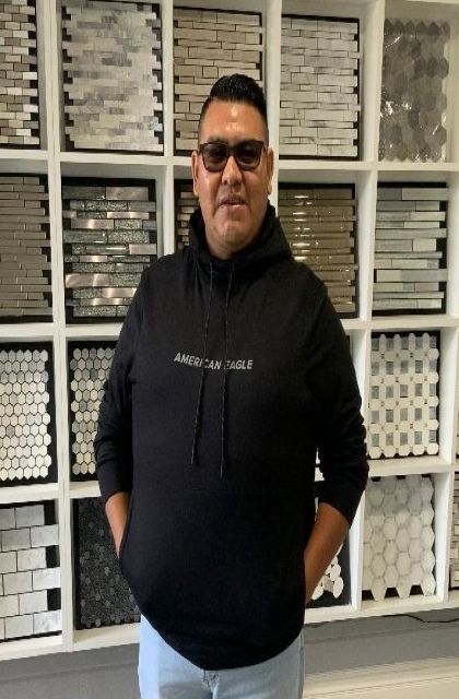 Man in black hoodie and sunglasses poses in front of tile samples.