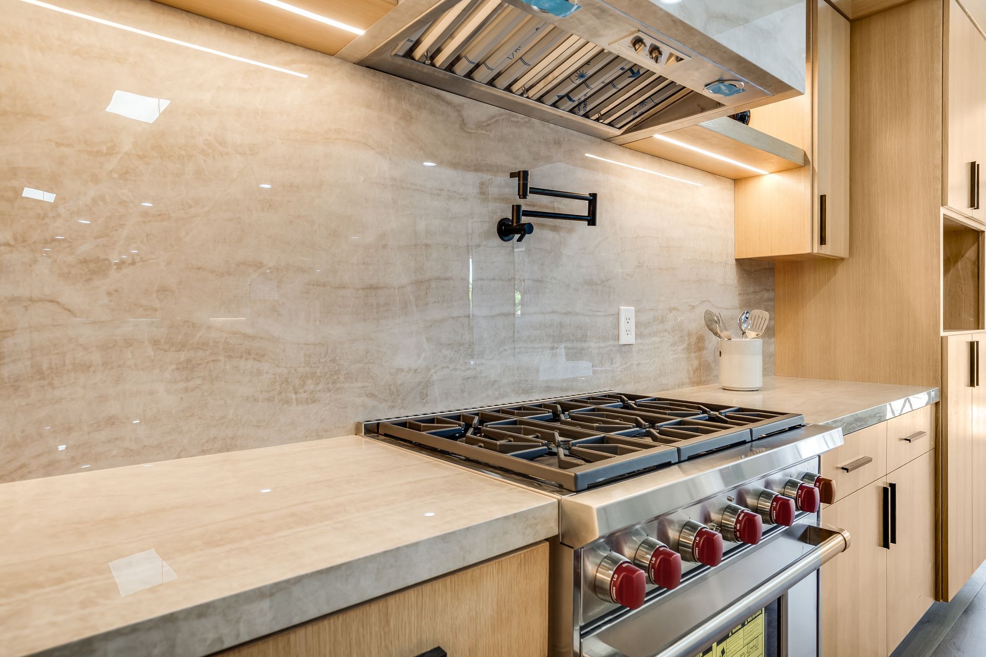 Modern kitchen with light wood cabinets, stone backsplash, and gas range.
