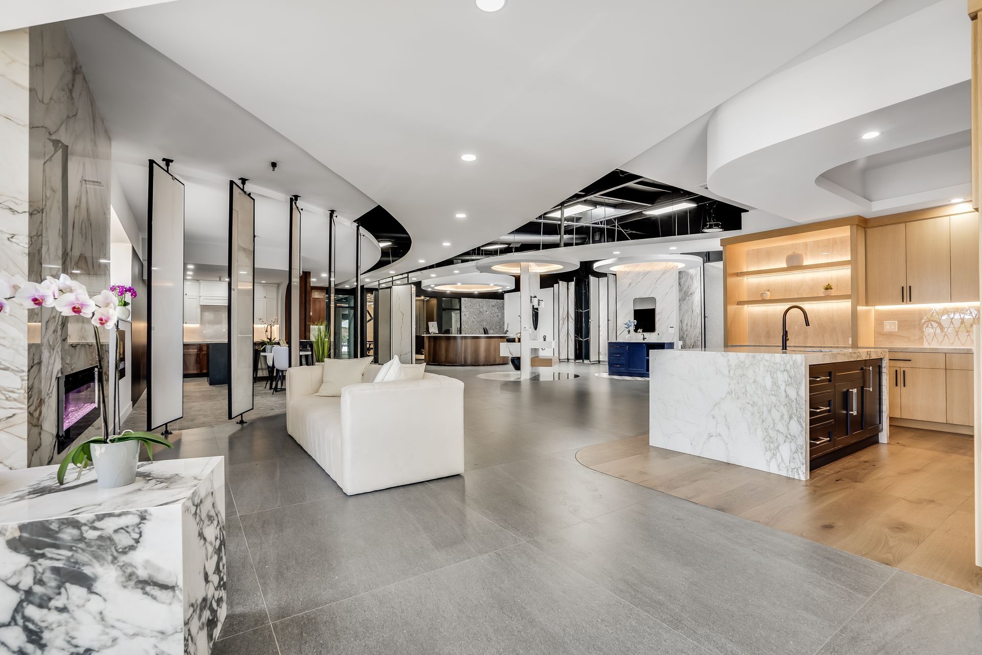 Spacious showroom with various kitchen and bathroom displays; white walls, marble, wood, and grey flooring.