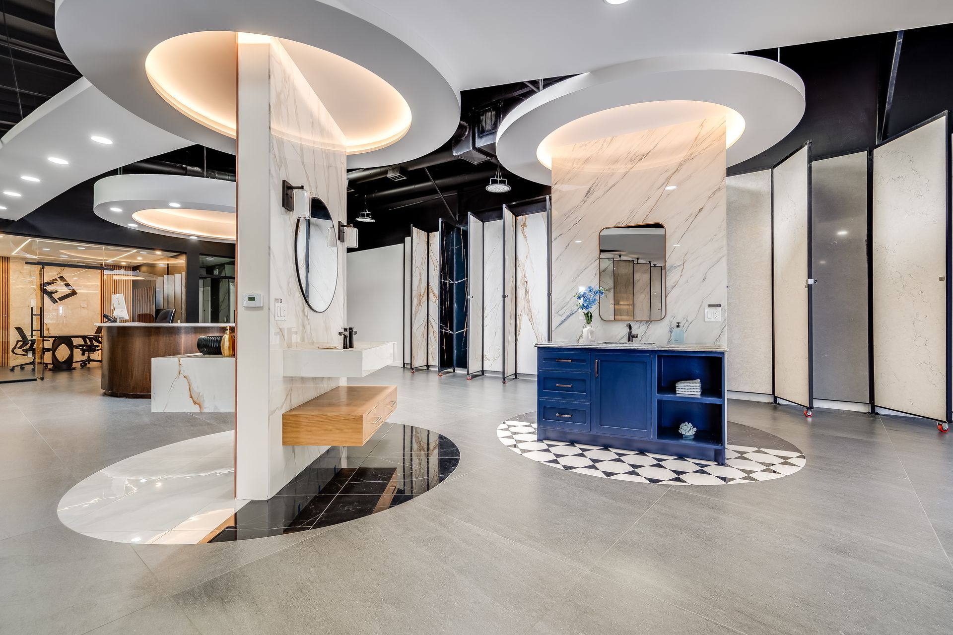 Reception desk in showroom. Curved brown base, light-colored top, computer, and two chairs under a circular recessed ceiling with lights.