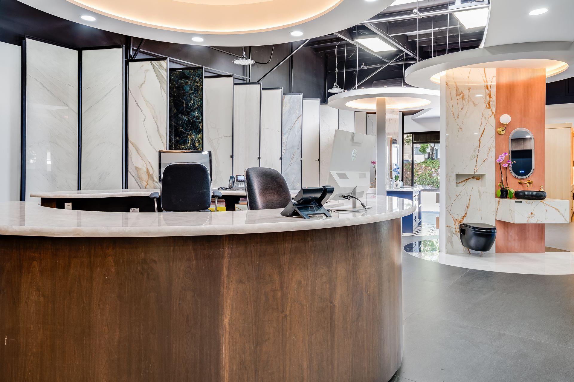 Reception area with a curved wooden desk, samples of tile, and a decorative wall.