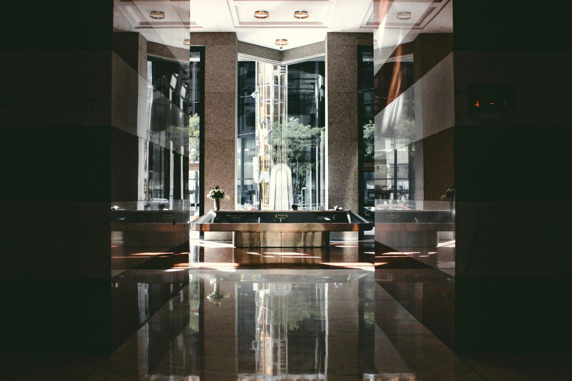 Interior of a modern building with a reflective floor. Large windows, a center structure, and geometric designs.