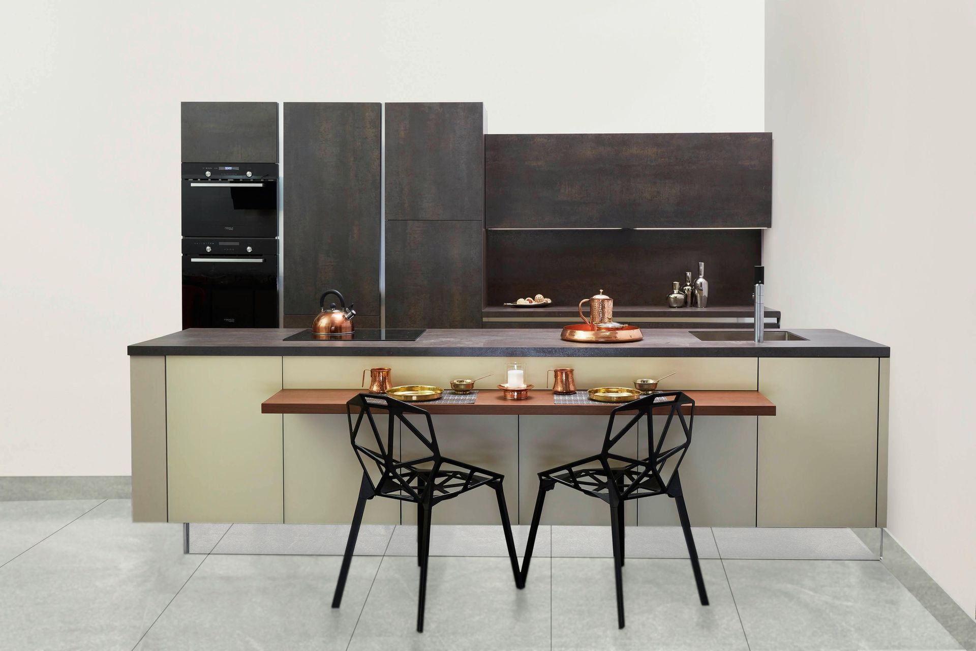 Modern kitchen with built-in appliances, metallic cabinets, a breakfast bar with two black chairs, and copper accents.