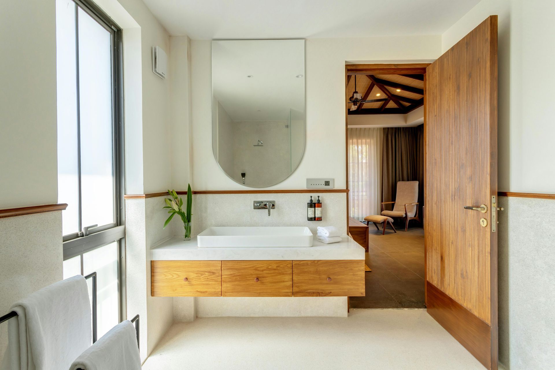 Bathroom with a floating wooden vanity, large mirror, and open door leading to a bedroom.