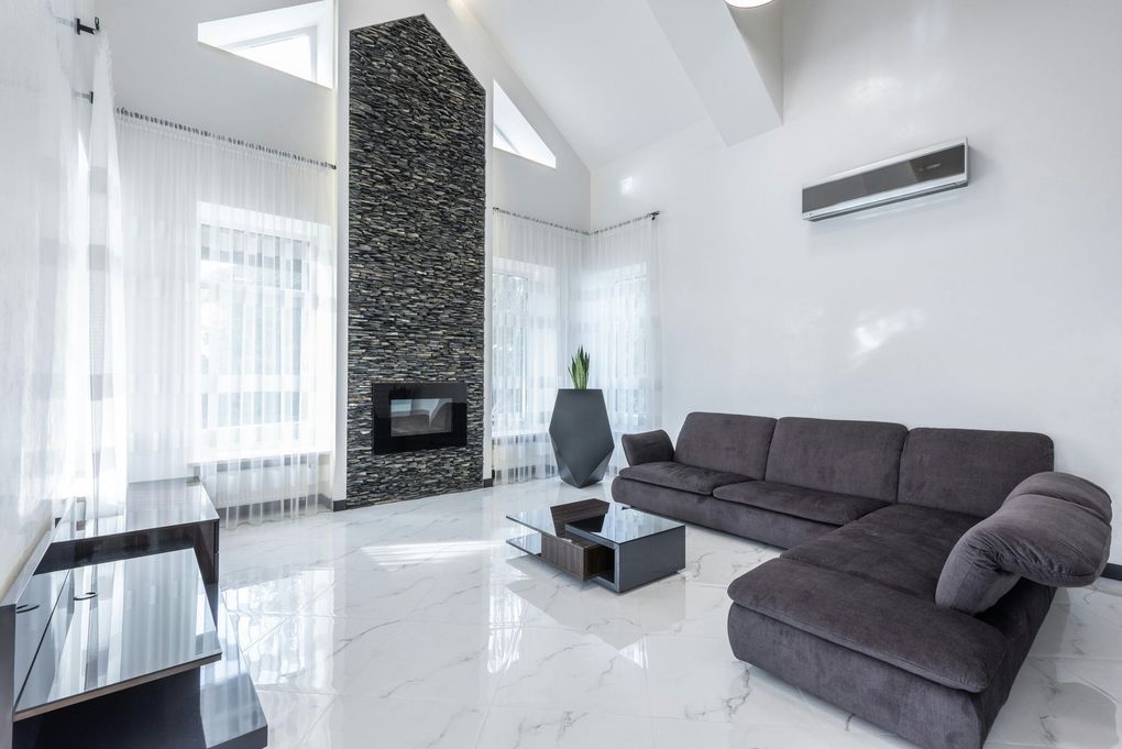 Modern living room with stone fireplace, gray sectional sofa, and large windows.