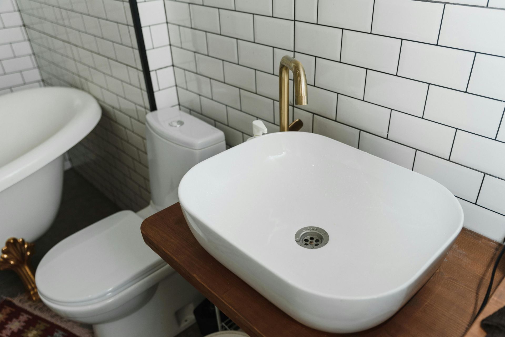 Bathroom with white sink and toilet, gold faucet, subway tile, and a white tub.